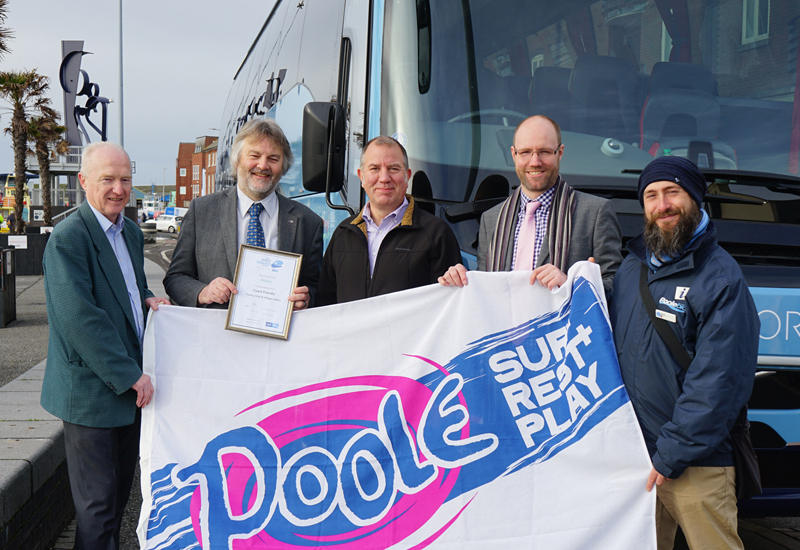 People holding flag in front of coach on Poole Quay